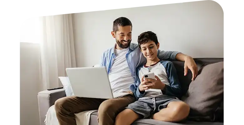 A father and son sit on couch and look at mobile device