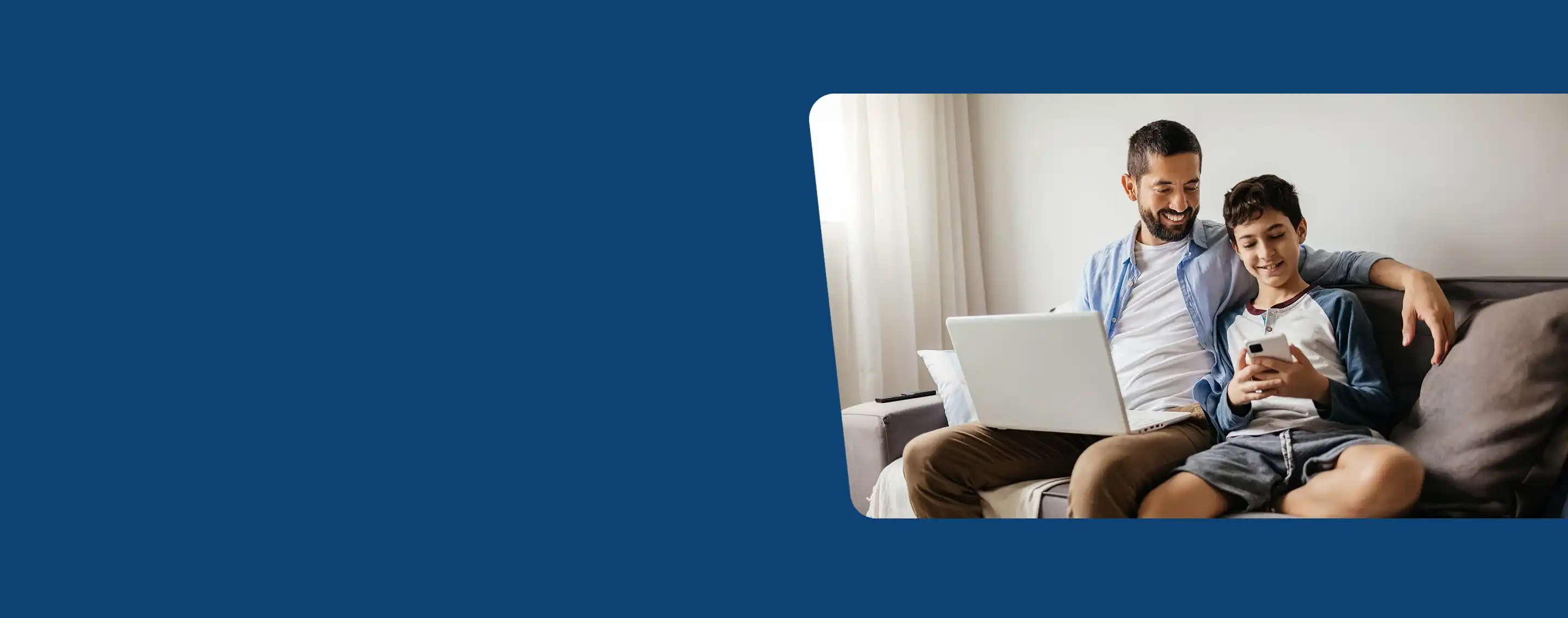 A father and son sit on couch and look at mobile device