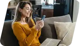 A woman browsing her phone with her laptop on her lap