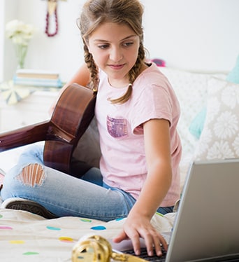 Young girl playing guitar and using laptop