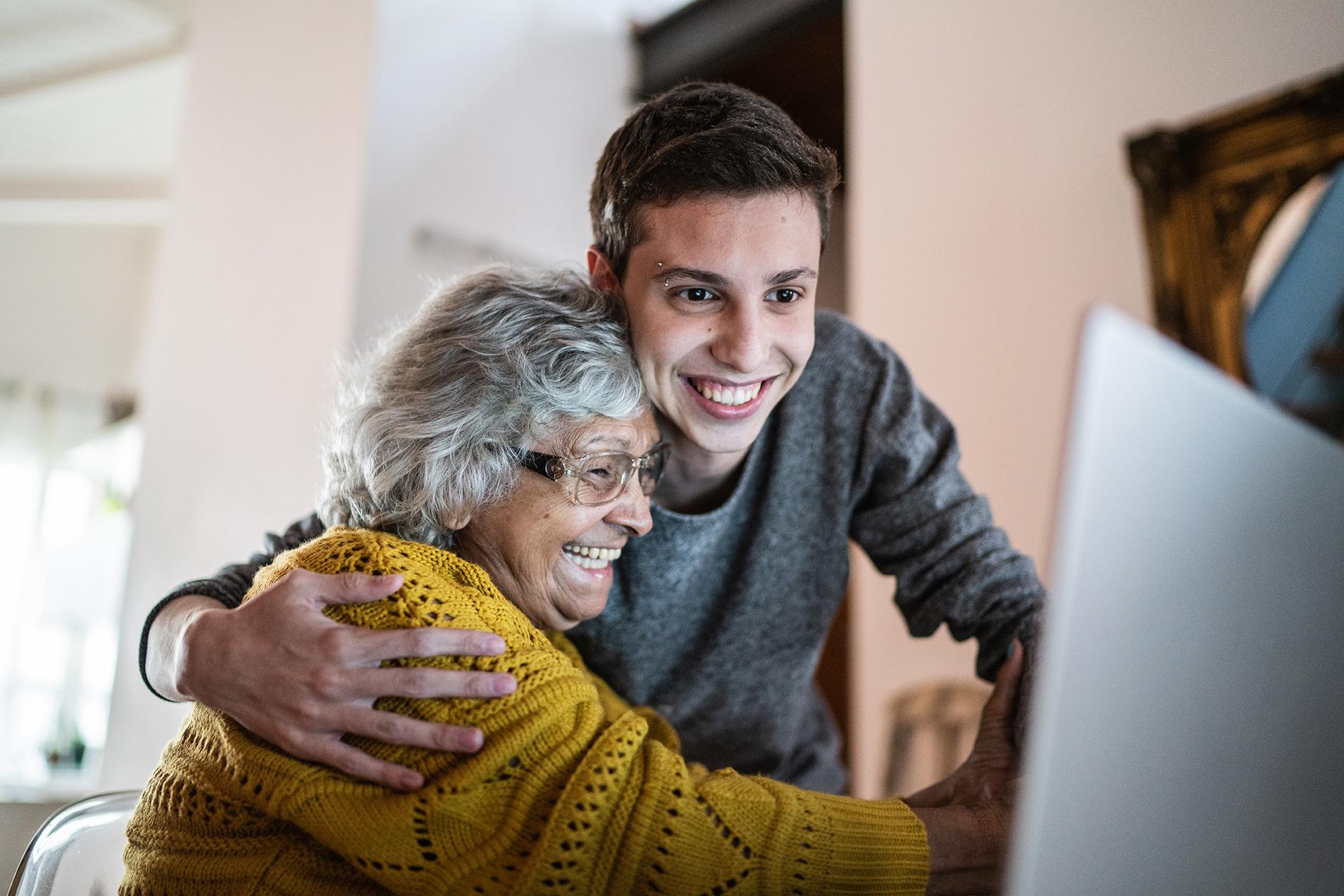 Smiling young man and elderly woman enjoying high-speed satellite internet on a laptop in a rural home.