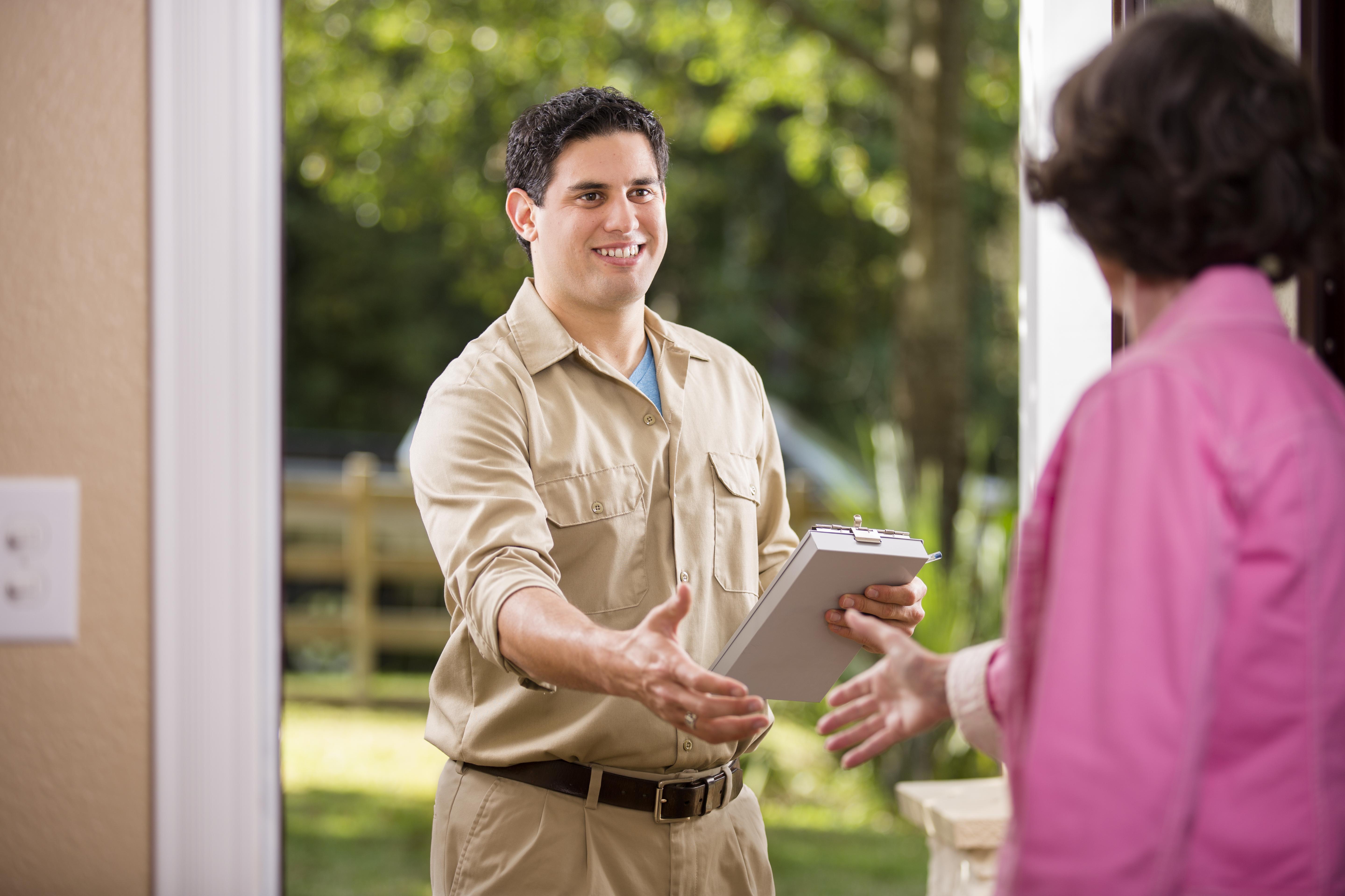 A friendly satellite internet technician in a tan uniform arrives at a customer's home, offering a handshake and holding a clipboard, ready to begin installation or service setup