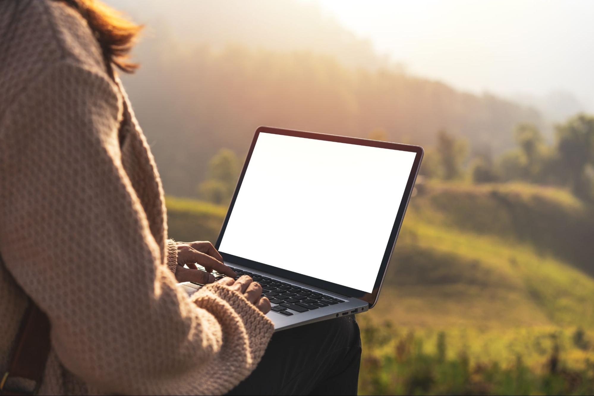 A woman looking at her laptop in a rural area. 